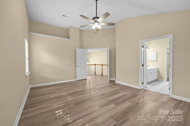 a view of an empty room with wooden floor and a ceiling fan