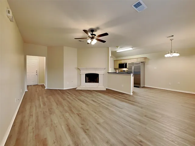 an empty room with wooden floor a ceiling fan a kitchen view and a fireplace