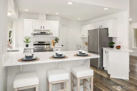 a kitchen with stainless steel appliances kitchen island granite countertop a sink a stove a refrigerator and white cabinets with wooden chairs