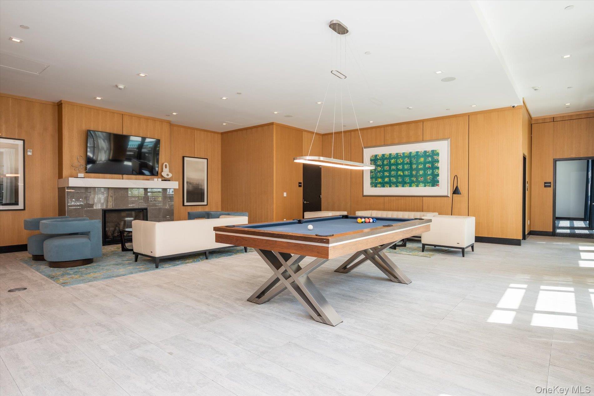 100 Garvies Point Road, Unit 1042 Glen Cove, NY 11542 - Photo 30 of 33 Playroom featuring wood walls, a glass covered fireplace, and billiards