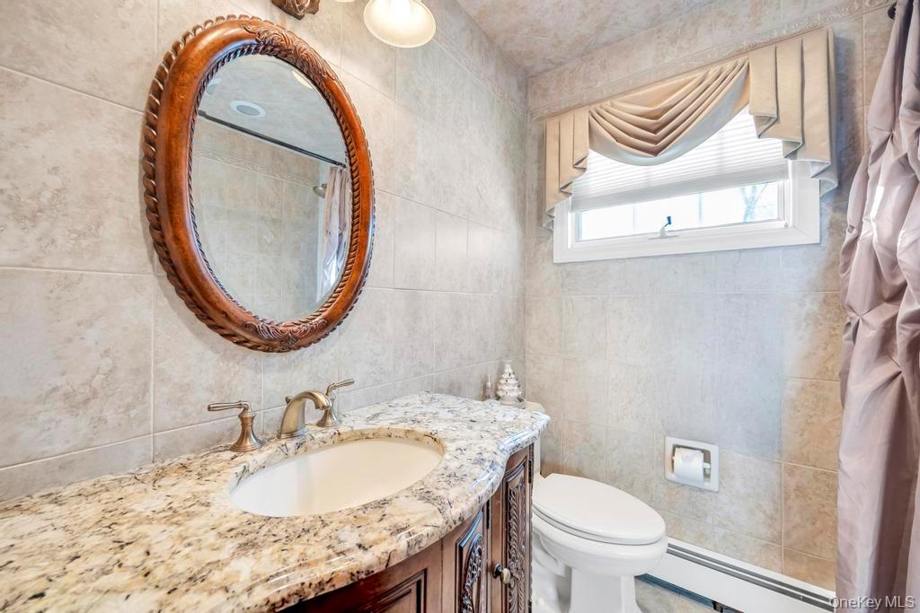 60 Essex Road Bethpage, NY 11714 - Photo 16 of 21 Full bathroom with curtained shower, baseboard heating, vanity, and tile walls