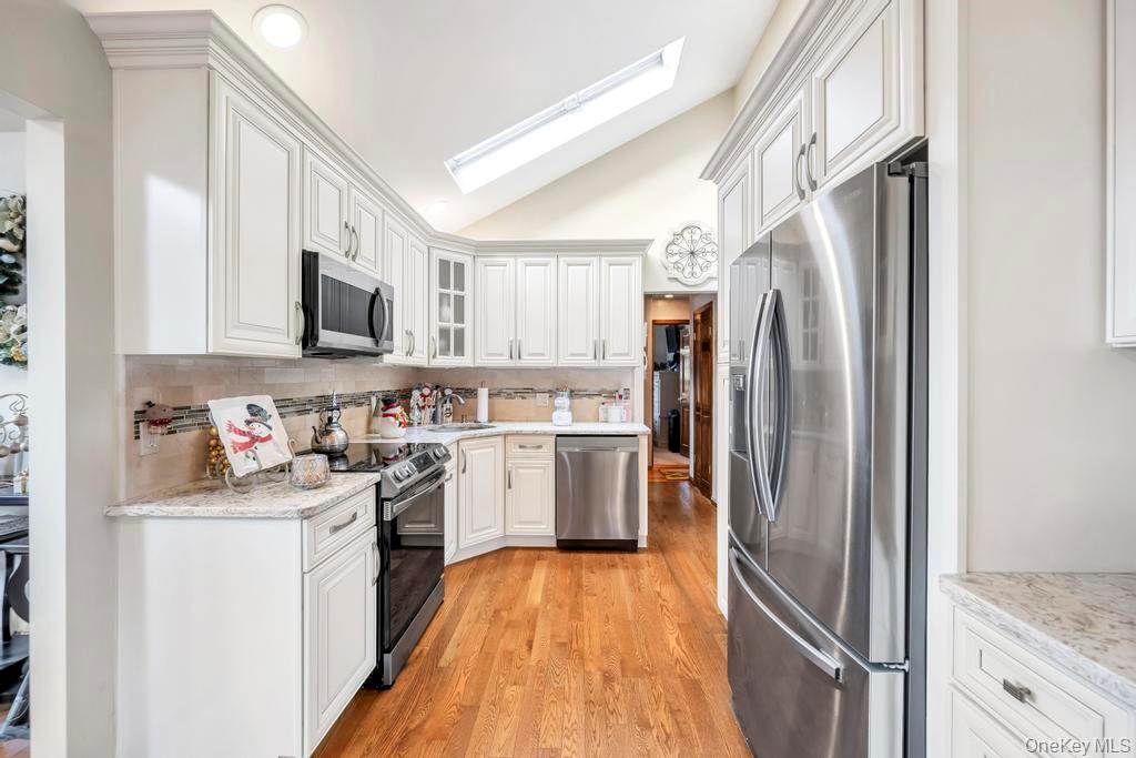 60 Essex Road Bethpage, NY 11714 - Photo 3 of 21 Kitchen with stainless steel appliances, white cabinets, lofted ceiling, light stone countertops, and glass insert cabinets