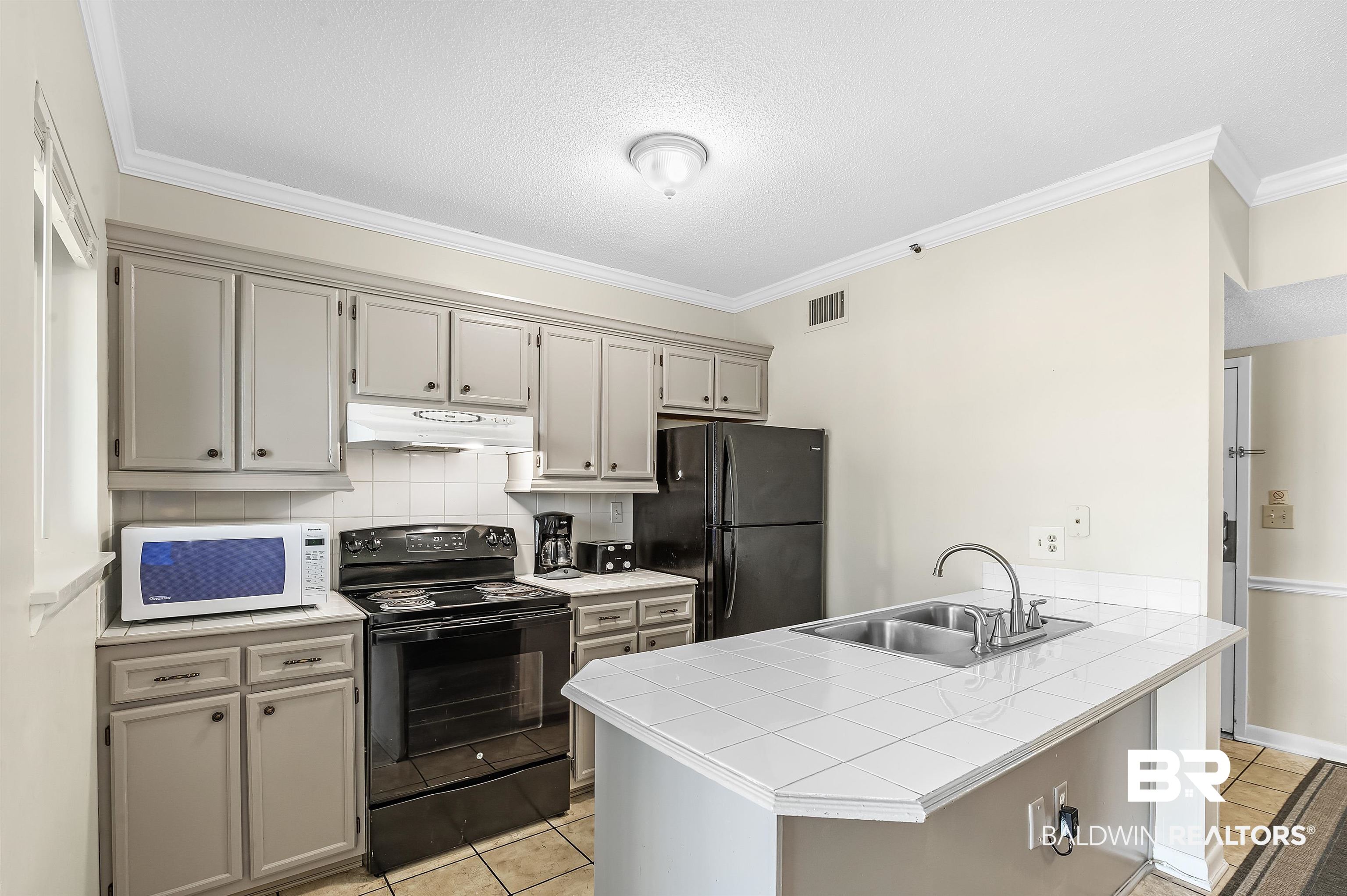 375 Plantation Road, Unit 5409 Gulf Shores, AL 36542 - Photo 11 of 48 Kitchen featuring light tile patterned flooring, crown molding, kitchen peninsula, black appliances, and sink