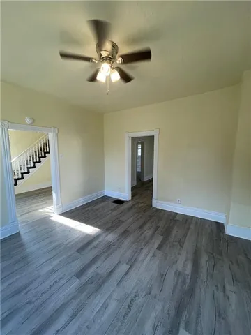 a view of an empty room with wooden floor and a ceiling fan