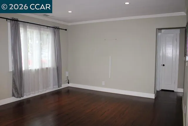 a view of an empty room with wooden floor & window