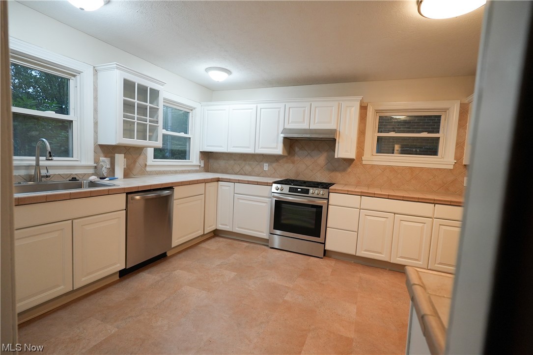 664 Ecton Road Akron, OH 44303 - Photo 10 of 35 Kitchen featuring backsplash, light countertops, appliances with stainless steel finishes, white cabinetry, and light tile flooring