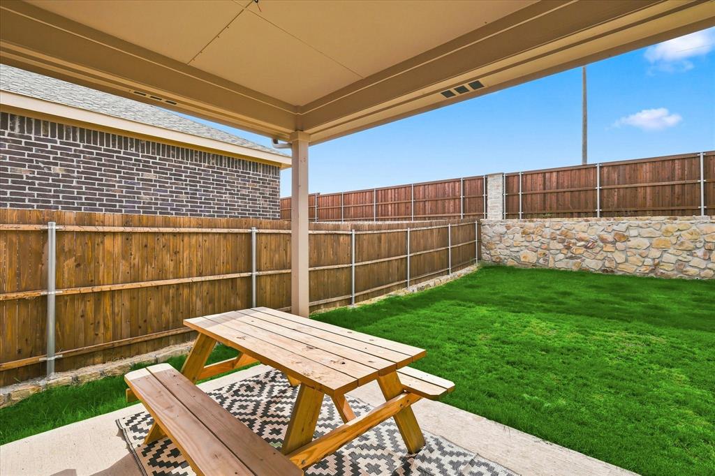 141 Medina Lane Rhome, TX 76078 - Photo 27 of 36 Covered patio with concrete flooring, private wood fencing, stone retaining wall, and an expansive lawn area