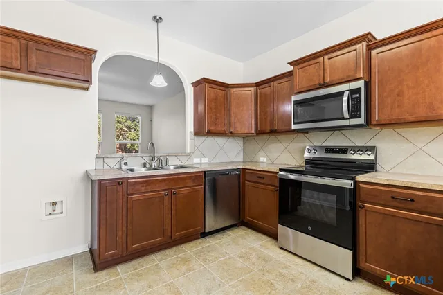 a kitchen with stainless steel appliances granite countertop a sink a stove a microwave and wooden cabinets