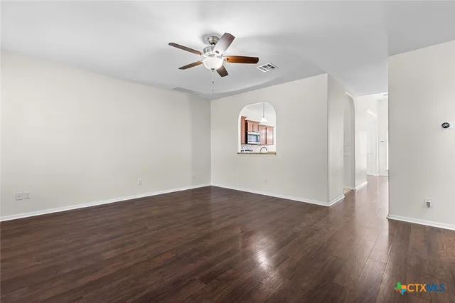 a view of an empty room with wooden floor and a ceiling fan