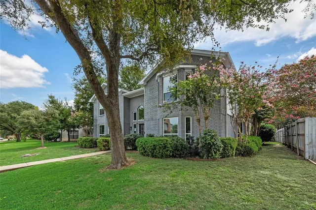 a view of a white house next to a yard with big trees