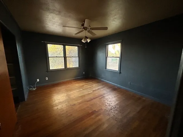 an empty room with wooden floor fan and windows