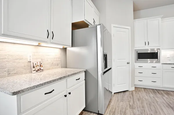 a large kitchen with stainless steel appliances granite countertop a stove a refrigerator a sink and white cabinets with wooden floor