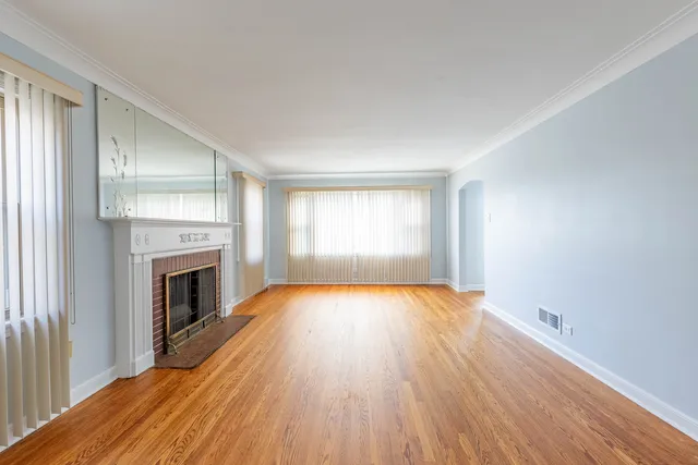 an empty room with wooden floor fireplace and windows