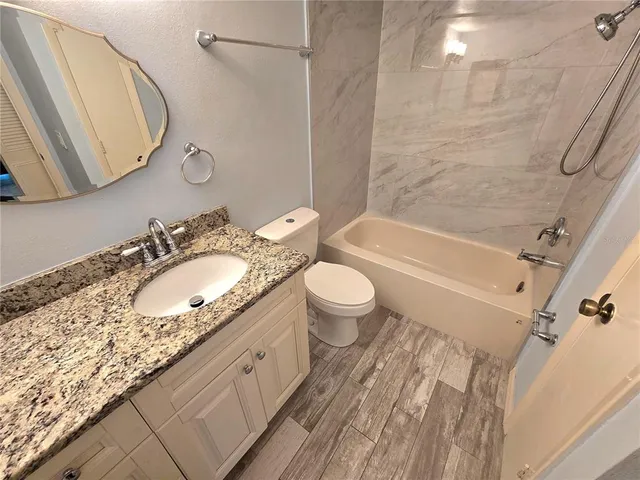 a bathroom with a granite countertop bathtub shower sink vanity and toilet