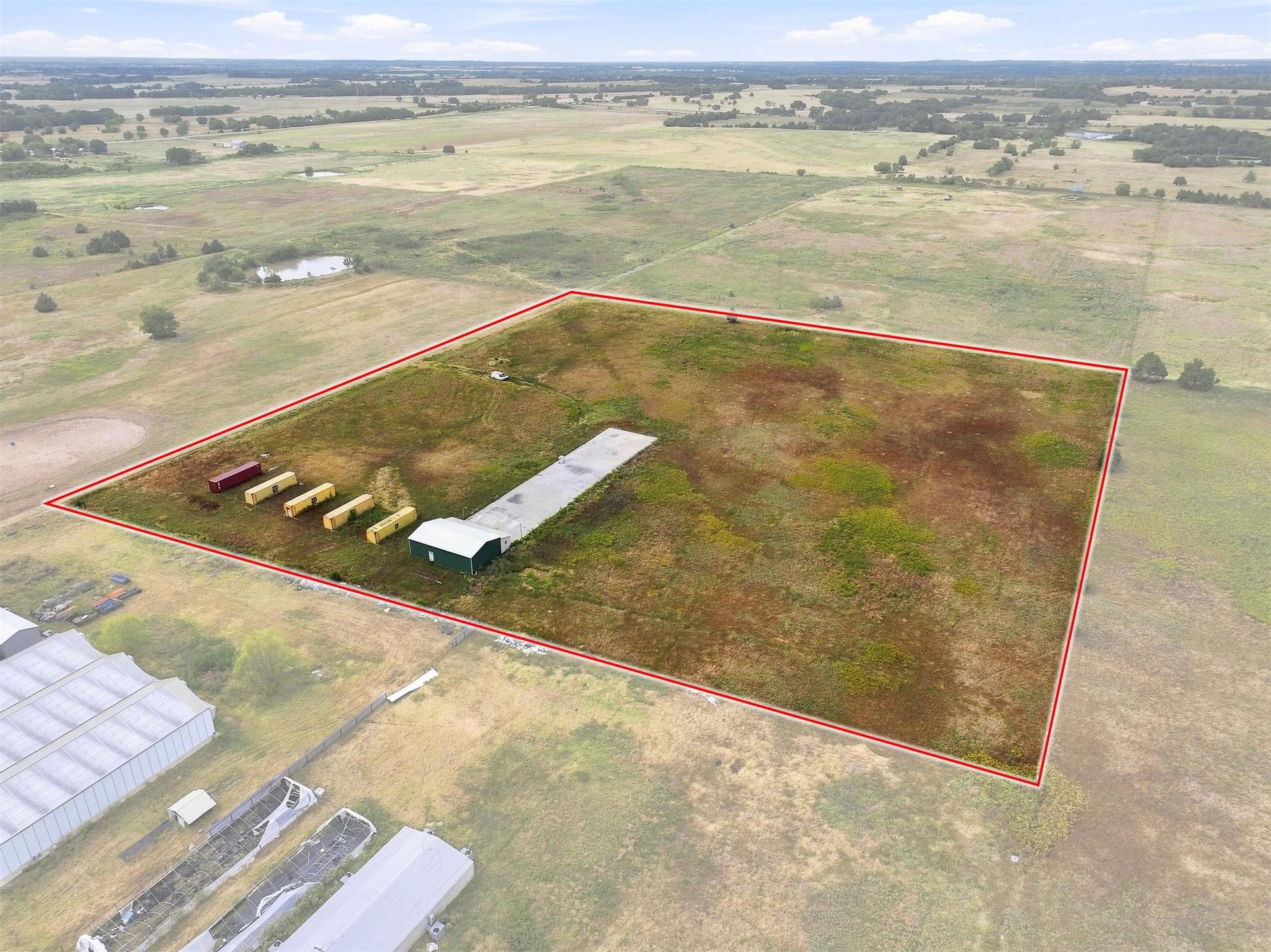 180 Tower Road Bokchito, OK 74726 - Photo 20 of 49 Expansive land parcel with a green outbuilding, multiple yellow storage containers, and a long concrete pad