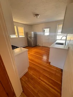 a view of kitchen and empty room with wooden floor
