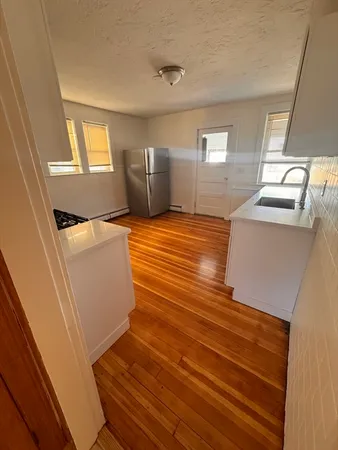 a view of kitchen and empty room with wooden floor