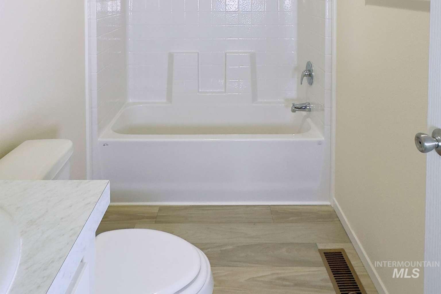 10 Kamloop Lane Orofino, ID 83544 - Photo 11 of 17 Bathroom featuring a white tub and shower combination with chrome fixtures, wood-finish flooring, a white toilet, and a vanity with a white countertop