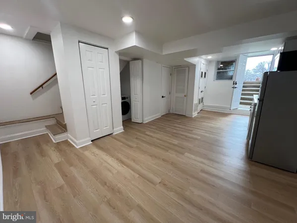 a view of a refrigerator in kitchen and an empty room with wooden floor