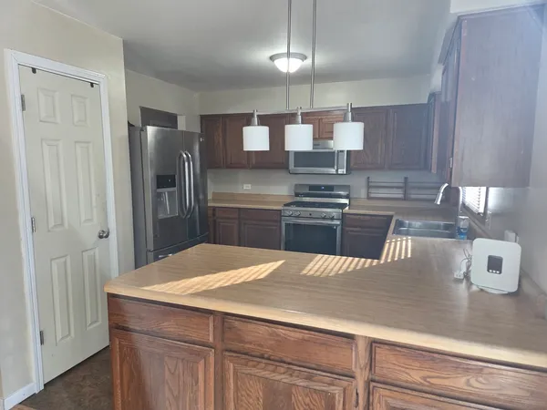 a kitchen with stainless steel appliances kitchen island granite countertop a refrigerator a sink dishwasher a stove and a dining table with wooden floor
