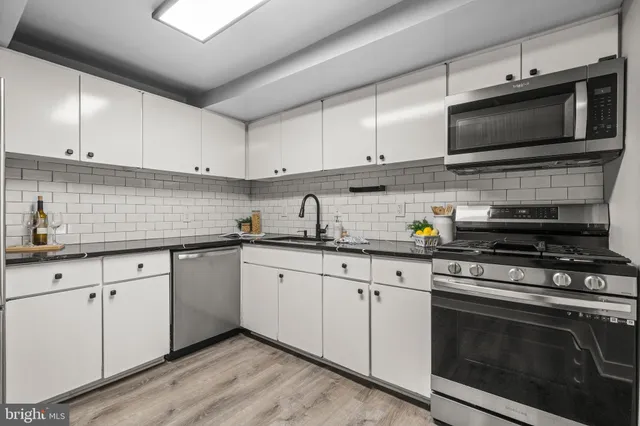 a kitchen with stainless steel appliances granite countertop a sink a stove top oven and white cabinets