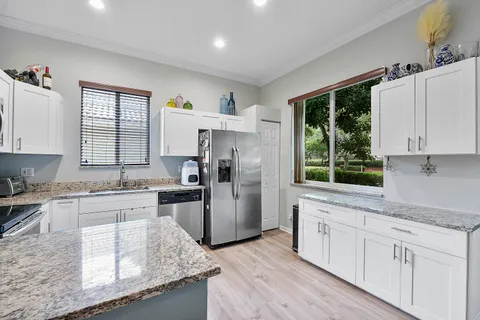 a kitchen with stainless steel appliances granite countertop a stove a sink dishwasher a refrigerator and white cabinets with wooden floor