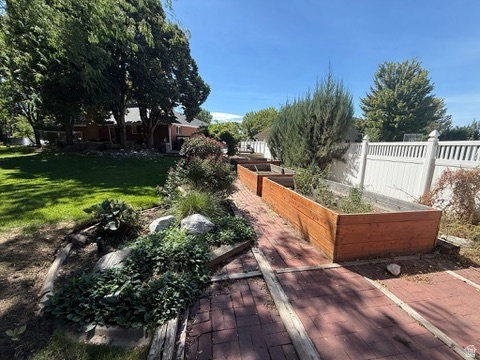340 Willow Ridge Circle Centerville, UT 84014 - Photo 29 of 32 Expansive backyard featuring a manicured lawn, brick paver pathway, multiple raised garden beds, established landscaping, and a white privacy fence