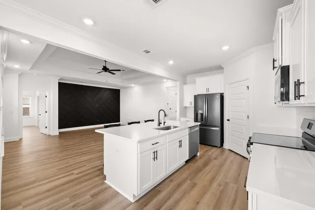 a kitchen with stainless steel appliances a stove top oven a refrigerator a sink and white cabinets with wooden floor