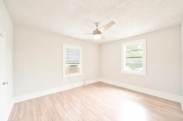 an empty room with wooden floor ceiling fan and windows