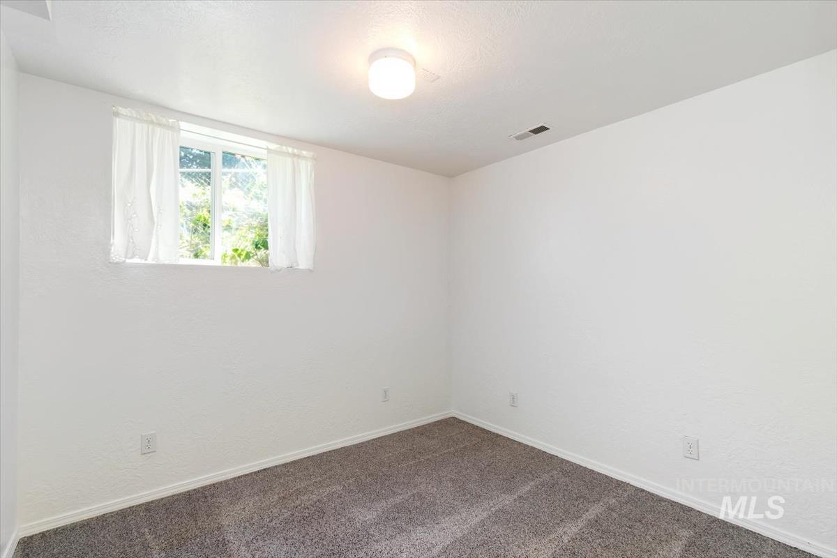 10178 West Fox Ridge Drive Boise, ID 83709 - Photo 25 of 36 Room featuring textured white walls, a single window with white curtains, recessed lighting, and grey carpeting