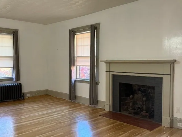 an empty room with wooden floor fireplace and windows