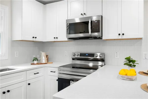 a kitchen with stainless steel appliances kitchen island granite countertop a stove a sink a microwave a refrigerator and white cabinets with wooden floor