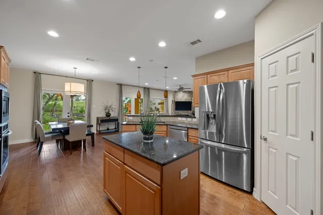 a kitchen with granite countertop stainless steel appliances a refrigerator a stove top oven and a dining table with wooden floor