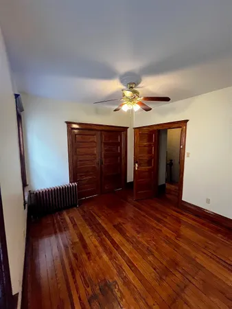 a view of an empty room with wooden floor and fan