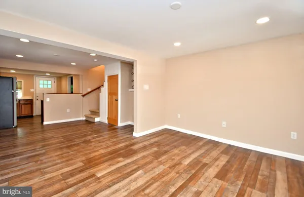 a view of an empty room with wooden floor and a kitchen