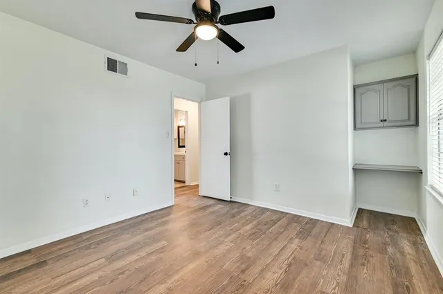 an empty room with wooden floor ceiling fan and windows