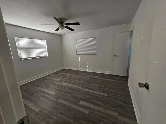 a view of an empty room with wooden floor and a ceiling fan