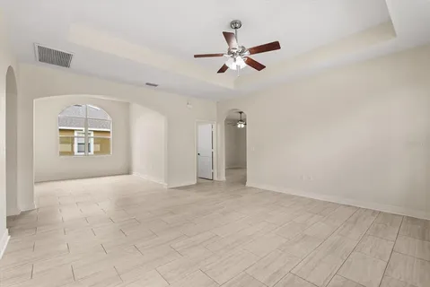 an empty room with chandelier fan and windows