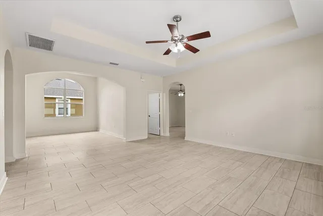 an empty room with chandelier fan and windows