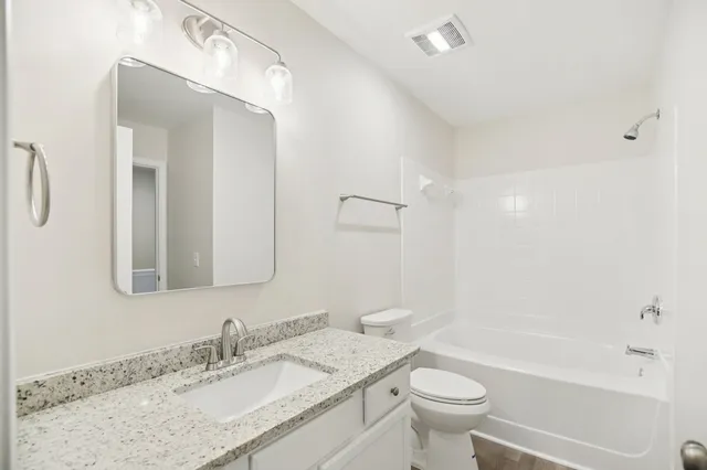 a bathroom with a granite countertop sink a toilet a mirror and shower