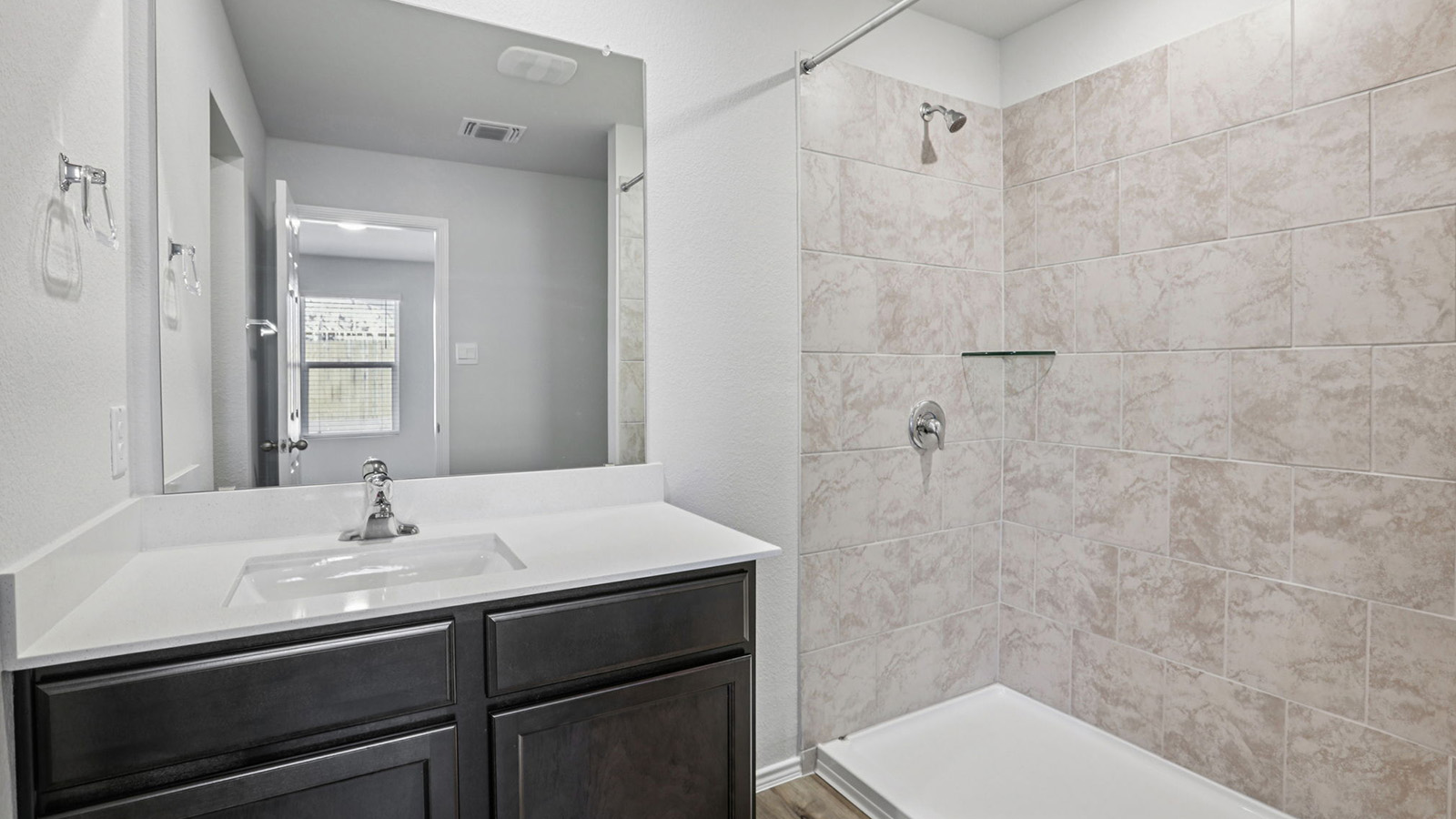 156 Wyatt Way Jarrell, TX 76537 - Photo 20 of 30 Bathroom featuring a dark wood-finish vanity with a white countertop and integrated sink, a large wall-mounted mirror, a tiled shower enclosure with a glass shelf, and a chrome shower fixture