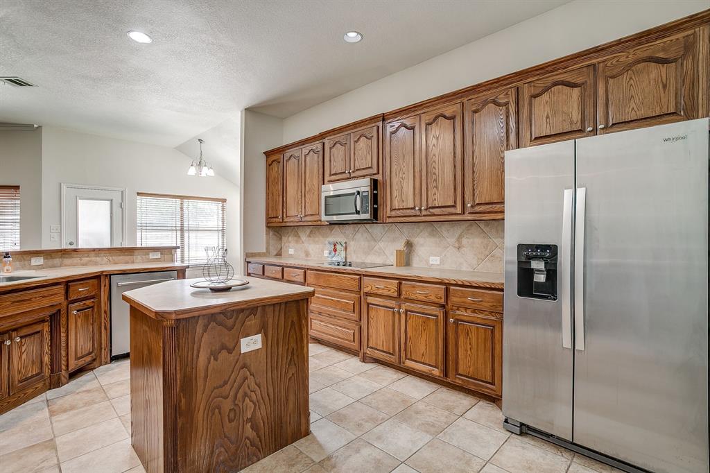 209 Cooperstown Drive Springtown, TX 76082 - Photo 17 of 40 Kitchen featuring appliances with stainless steel finishes, brown cabinets, tasteful backsplash, a kitchen island, and light countertops