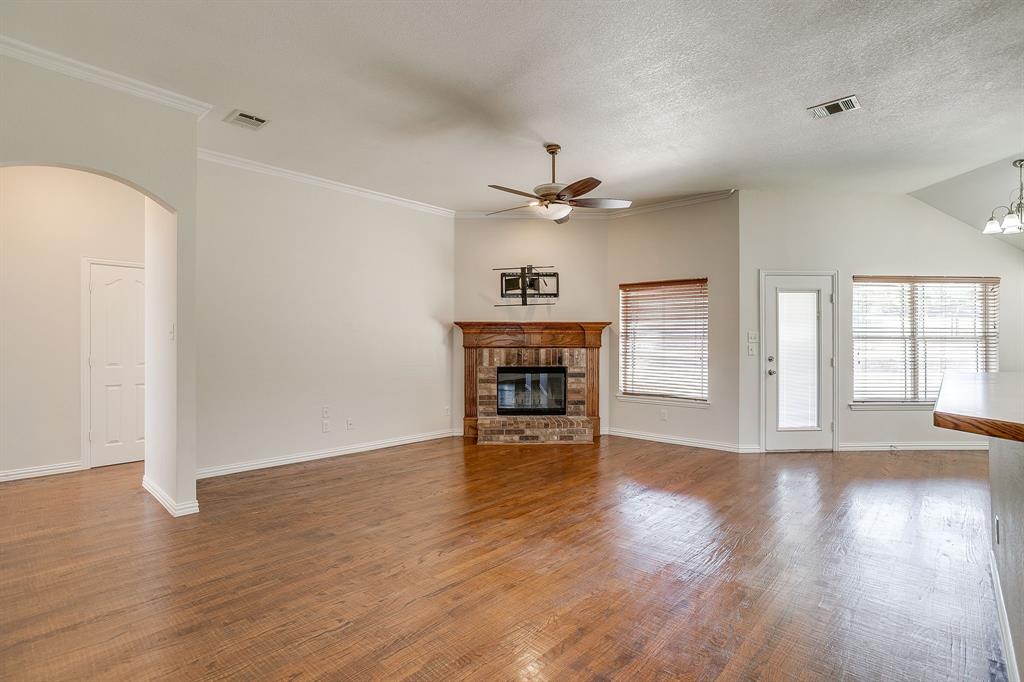 209 Cooperstown Drive Springtown, TX 76082 - Photo 8 of 40 Unfurnished living room with a fireplace, wood finished floors, arched walkways, a ceiling fan, and a chandelier