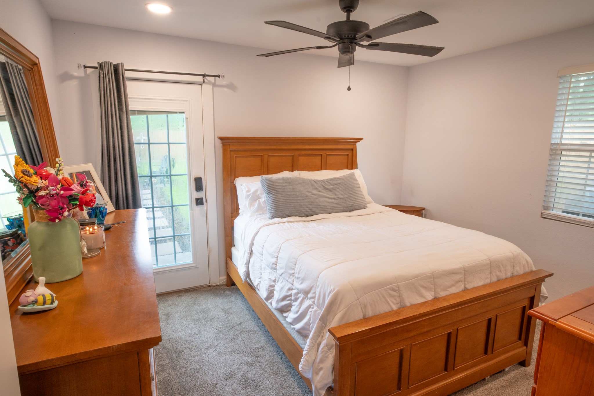 846 South Anderson Street Angleton, TX 77515 - Photo 15 of 30 Cozy primary bedroom with room for a queen size bed frame and matching furniture, featuring a ceiling fan and soft carpeting. Natural light enters through a window and a glass-paned door leading outside to the walkway headed to the firepit.