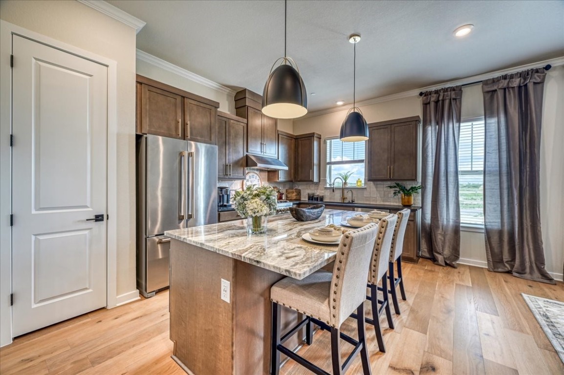 Kitchen featuring decorative light fixtures, light hardwood / wood-style floors, a kitchen island, high quality fridge, and dark brown cabinetry