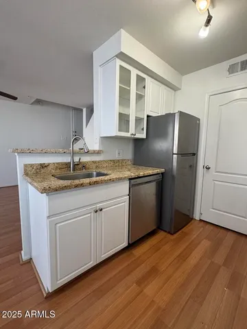 a kitchen with stainless steel appliances granite countertop a sink dishwasher a refrigerator and wooden floor