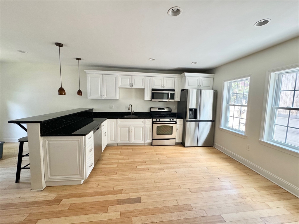 5 St James Place, Unit 5 Boston, MA 02119 - Photo 2 of 12 a large kitchen with granite countertop a stove a sink dishwasher a refrigerator and white cabinets with wooden floor