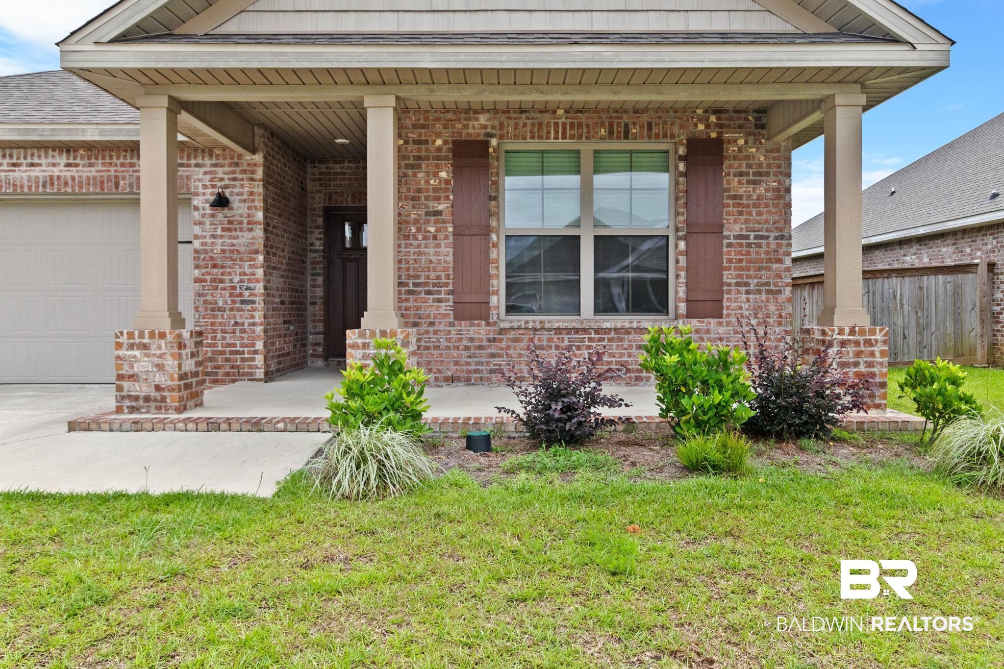 1710 Grouse Street Foley, AL 36535 - Photo 12 of 76 Brick exterior featuring a covered porch with column supports, a large window with shutters, an entry door, and an attached garage
