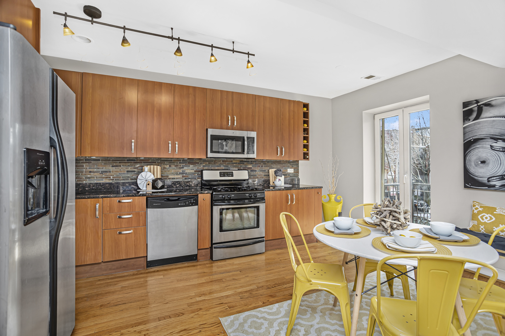1210 West Roscoe Street, Unit 1 Chicago, IL 60657 - Photo 7 of 20 a kitchen with stainless steel appliances kitchen island granite countertop a refrigerator a stove top oven and a dining table with wooden floor