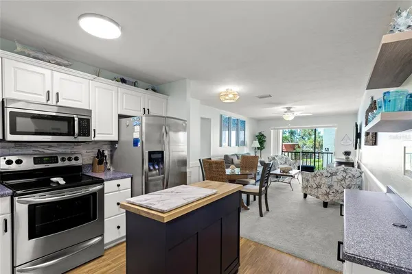 a kitchen with stainless steel appliances kitchen island granite countertop a stove top oven a sink dishwasher a dining table and chairs with wooden floor